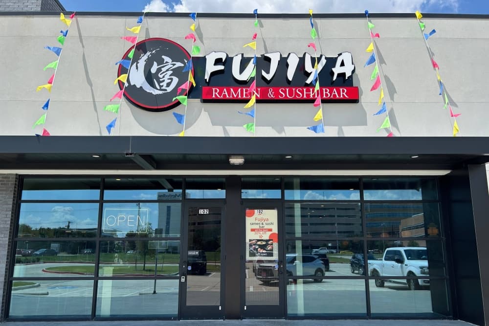 Exterior of a building with Fujiya Ramen Sushi Bar signage and multi-colored pennants strung across the top of the building. 