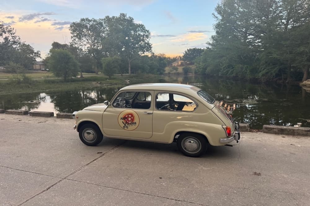 A vintage hatchback car next to a lake at sunset.