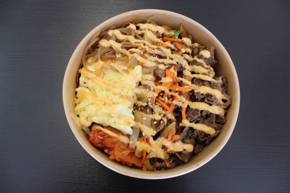 Egg, meat, vegetables in a bowl drizzled with light orange cream sauce. 
