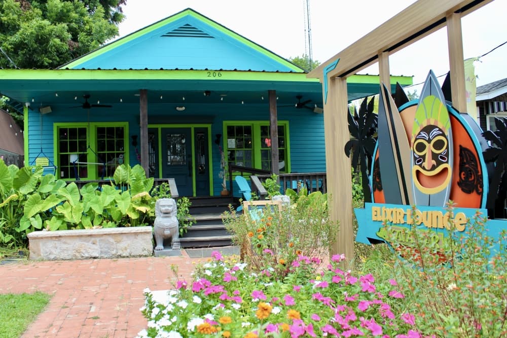 a green and blue building surrounded by a garden of flowers and greenery