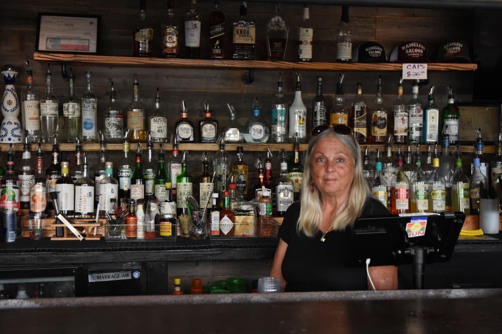 The image shows a woman standing behind a bar.