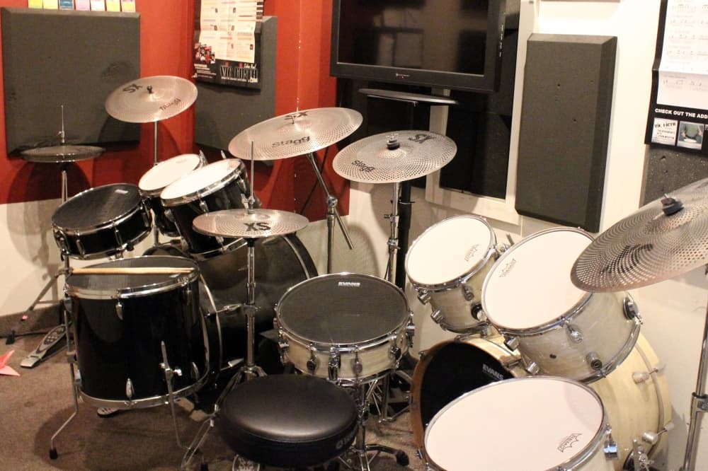 Two drum kits sitting side-by-side in a class room. 