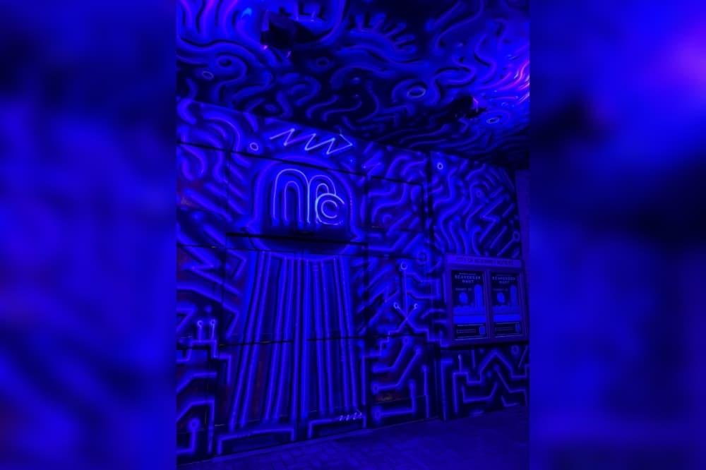 Blue graphic images painted on a black background on a building, at night and glowing