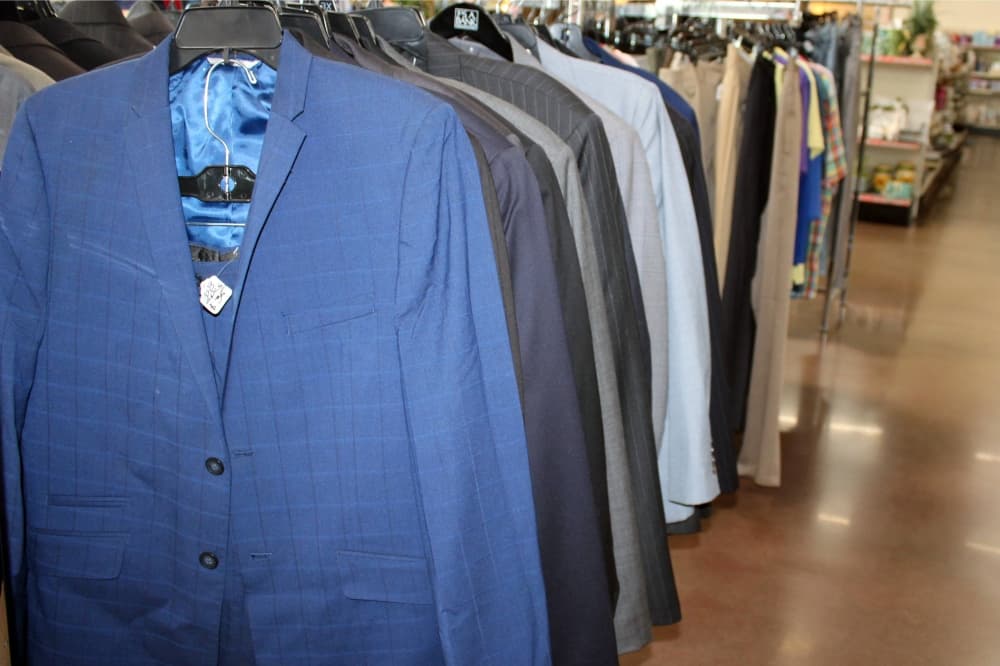 Blue man's suit hanging on a rack with other men's suits in a store. (Karen Chaney/Community Impact)