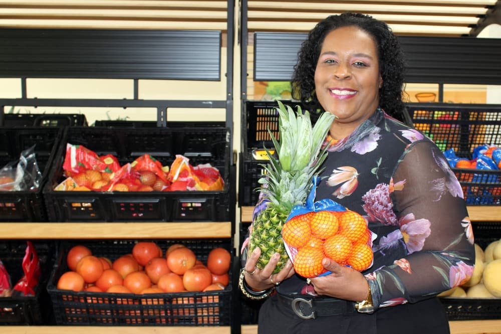 Female holding a bag of small oranges and pineapple while standing in front of a produce section in a store. 