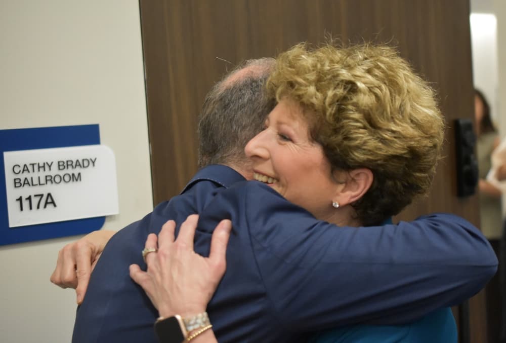 a woman is given a hug outside a room with a sign 