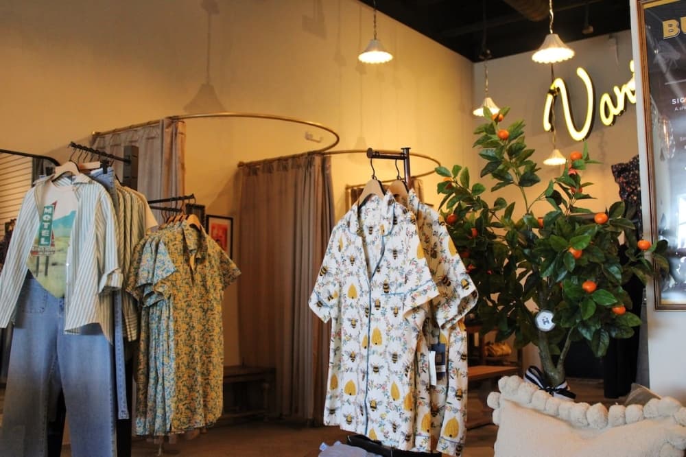 Racks of shirts and pants in a boutique next to an orange tree.
