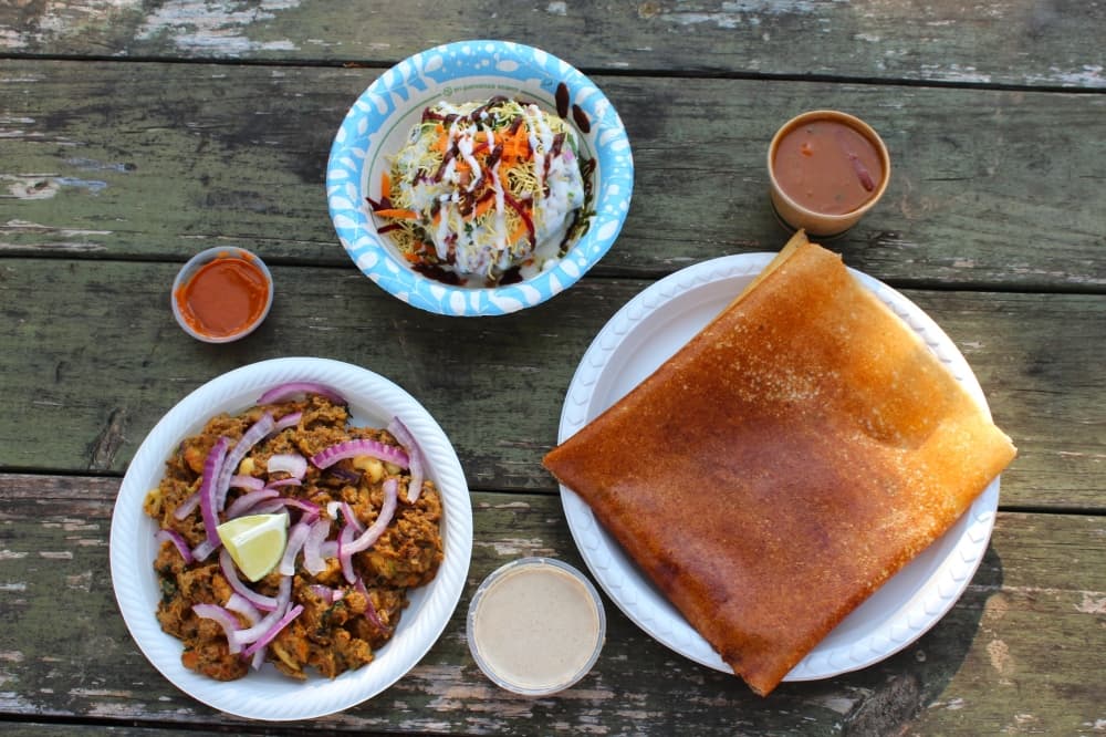 Pictured is mughlai murgh roast (bottom left), masala dosa with a potato filling (bottom right) and raj karchori, which is a hollow fried dough filled with vegetables and topped with a type of sour cream, (top middle). The masala dosa is served with a rich, savory dipping sauce, a peanut sauce and a stew. (Sienna Wight/Community Impact)