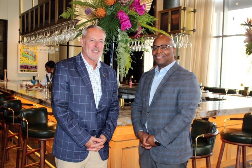 Two males wearing sports jackets standing next to each other in front of a bar. 