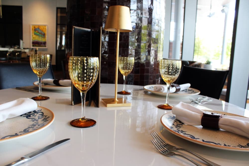 Table setting featuring white plates, light gold glasses and cloth napkins. 