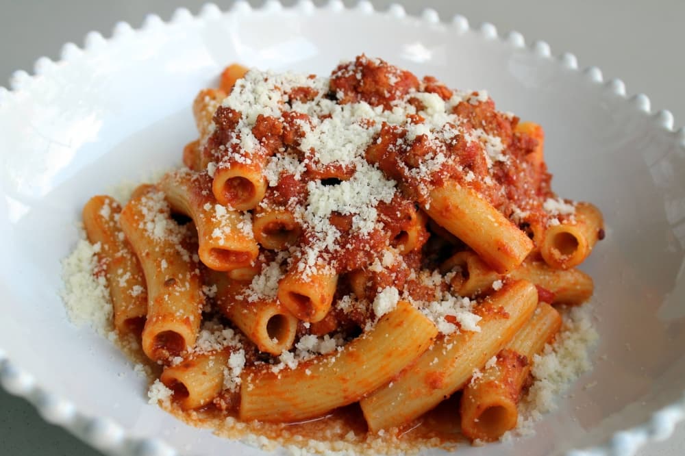 Pasta, meat sauce topped with cheese in a white bowl. 