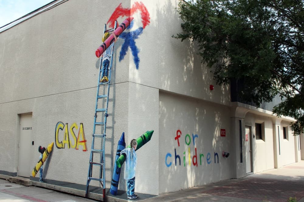 Children using crayons and a ladder depicted in mural on white building. 