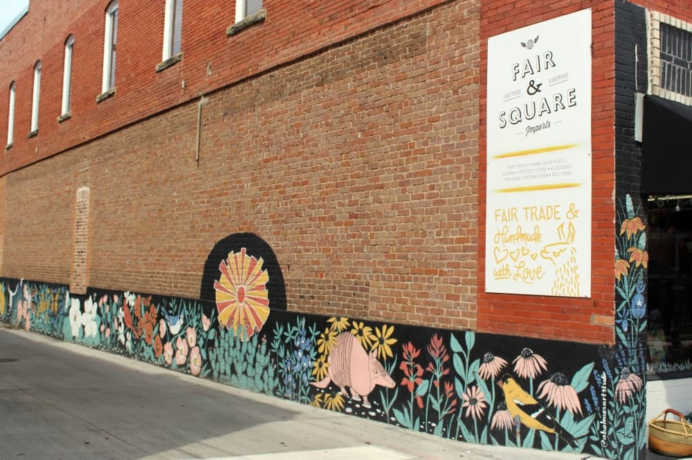 Exterior of a brick building with mural lining the bottom featuring flowers on black background. 