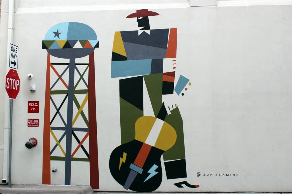 Abstract mural featuring cowboy holding a guitar and water tower. 