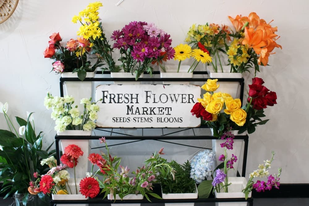 Various stems of flowers in a display featuring a Fresh Flowers Market sign. 