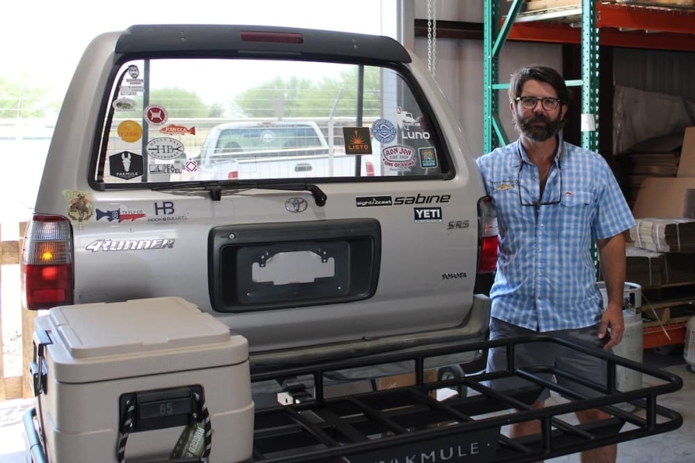 A business owner stands next to his product, an SUV storage carrier.