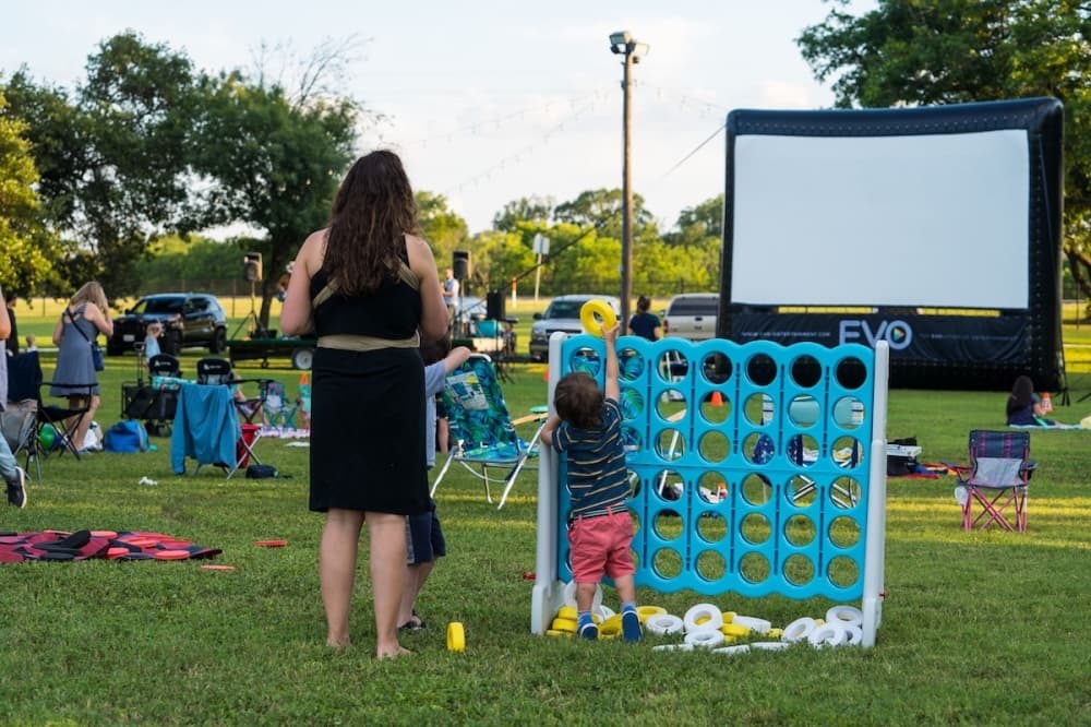 Children and parents play games before an outdoor movie at sunset.