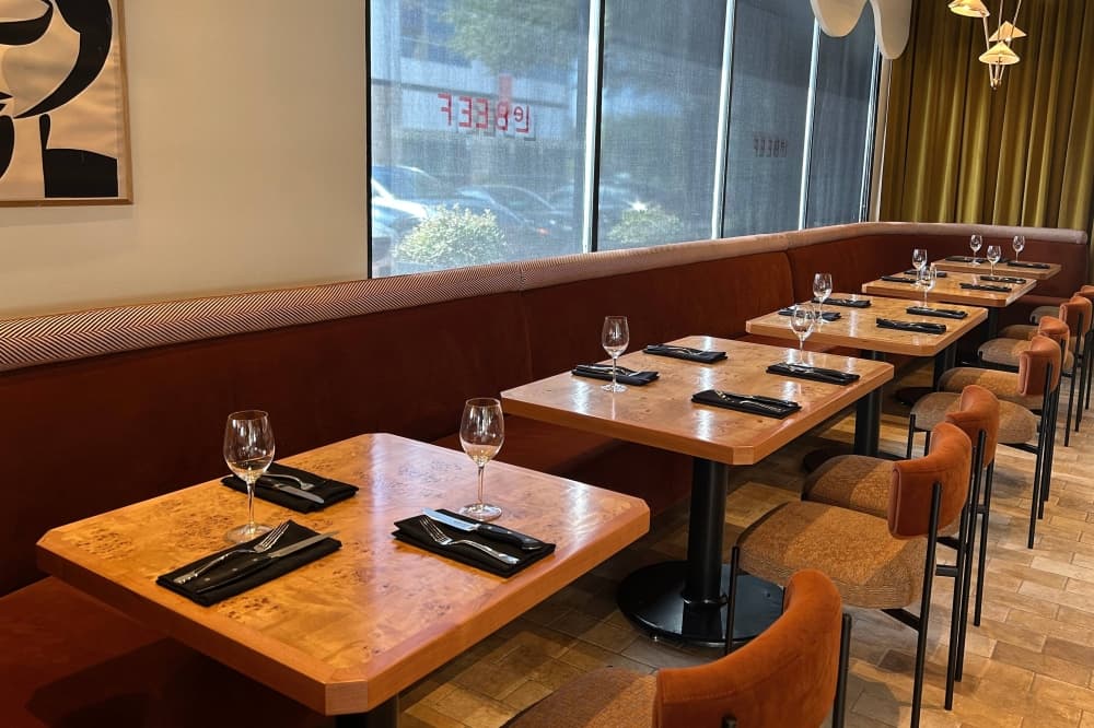 Interior of a restaurant with wooden square tables and dark red cushioned seats.