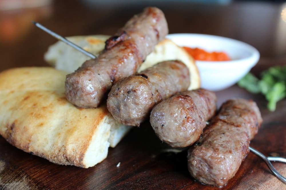 Four sausages on a skewer with sides of bread and red dipping sauce. 