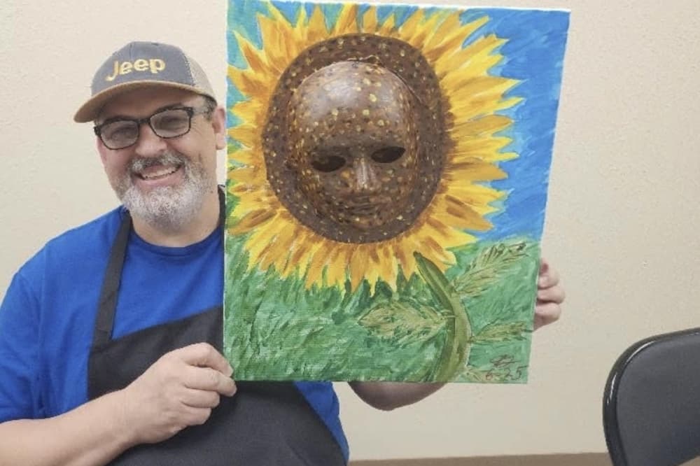 man holds up a painting of a sunflower