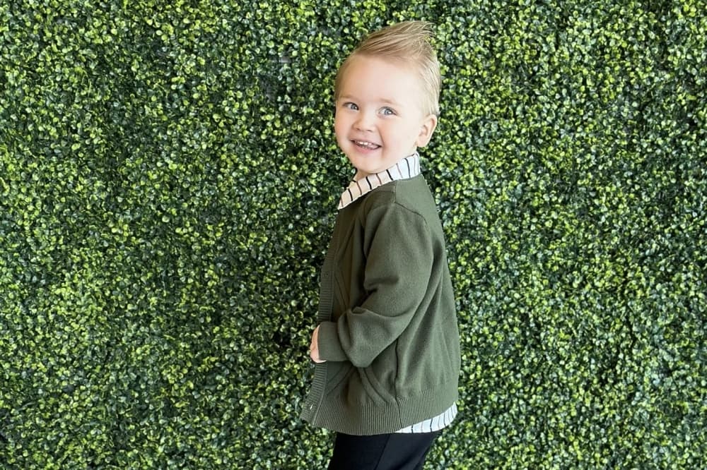 A boy in front of a grass wall