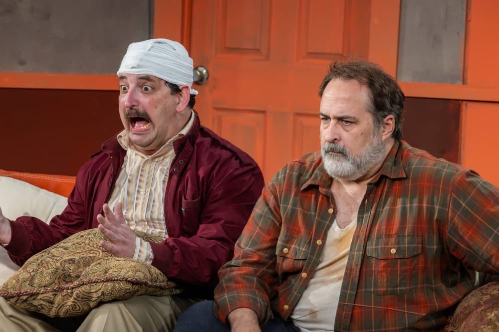 Two males sitting on a couch. One has a bandage on his head. 