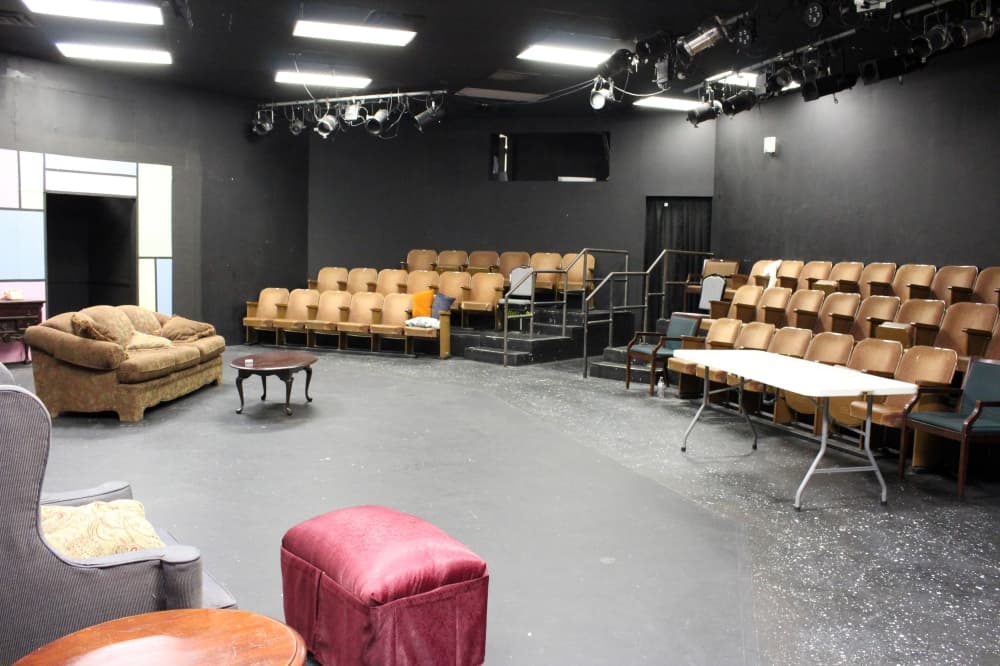 View from theater stage of furniture on a set and audience seating on risers.