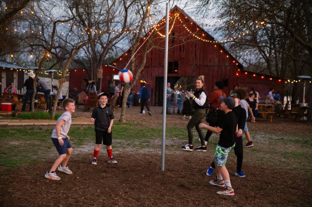 Males playing tether ball in front of a red barn. 