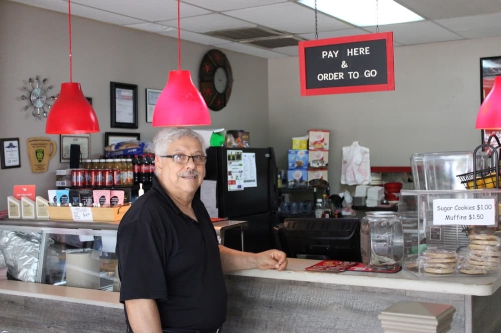 a man wearing a black shirt and glasses stands near an ordering counter