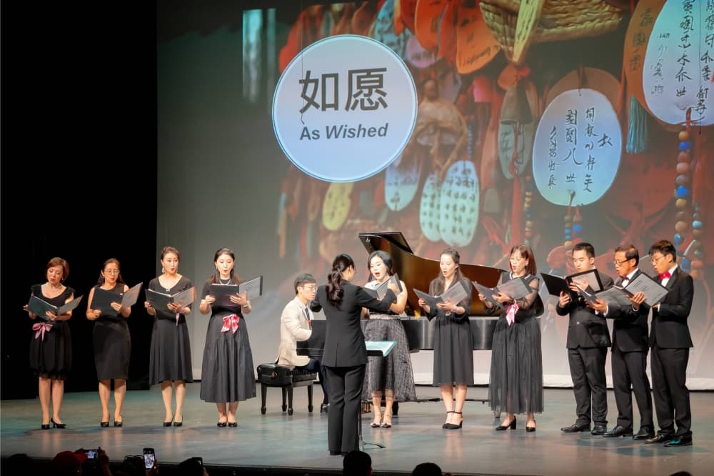 Adult females and males perform on stage with a pianist accompanist. 