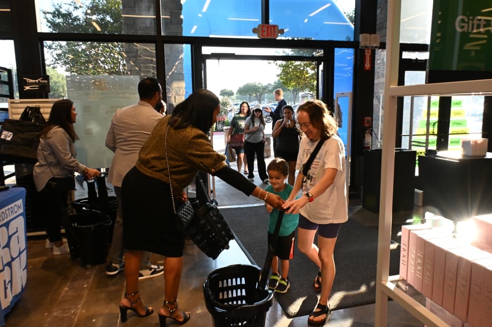 Nordstrom Rack employees hand carts to shoppers as they walk into the store.