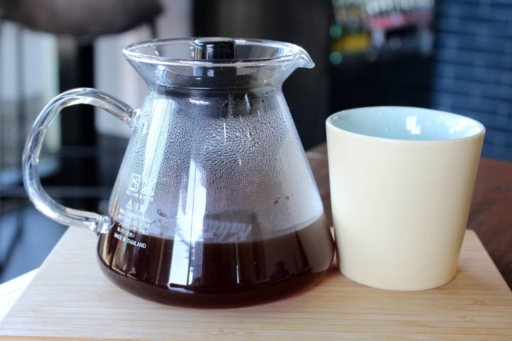 Individual coffee pot with coffee next to a handleless coffee cup. 