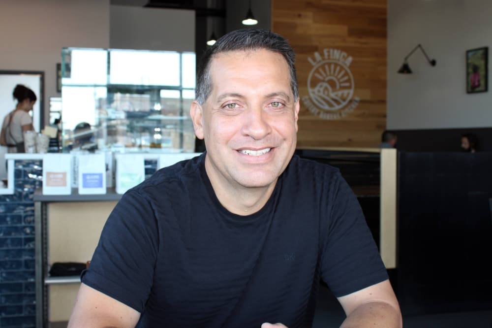Male sitting at a table in a restaurant with La Finca Coffee, Bakery, Kitchen signage on a wall in the background. 