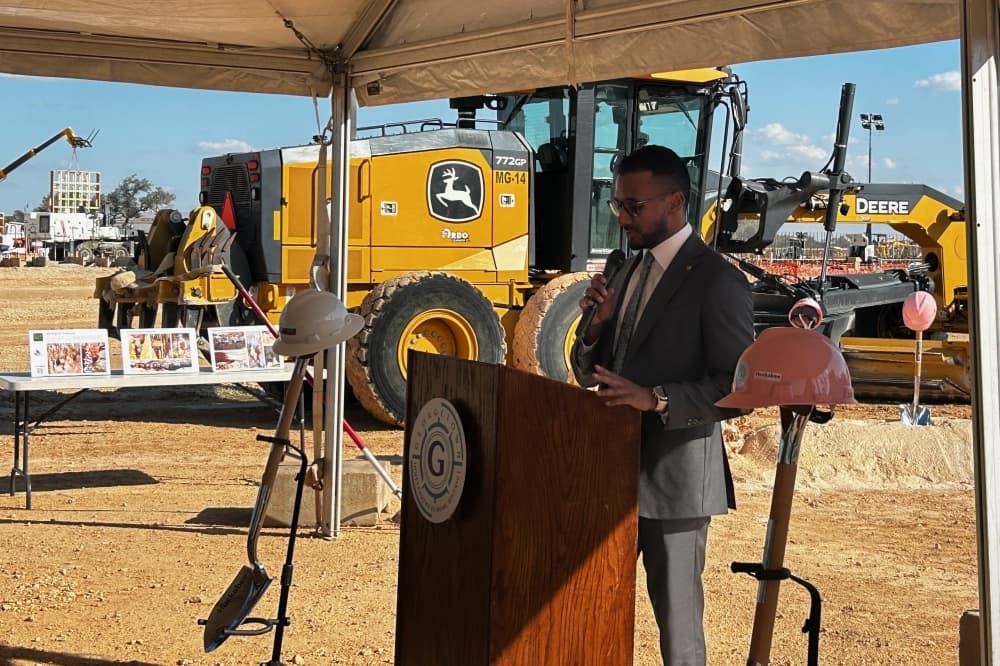a man speaks at a podium with construction equipment in the background
