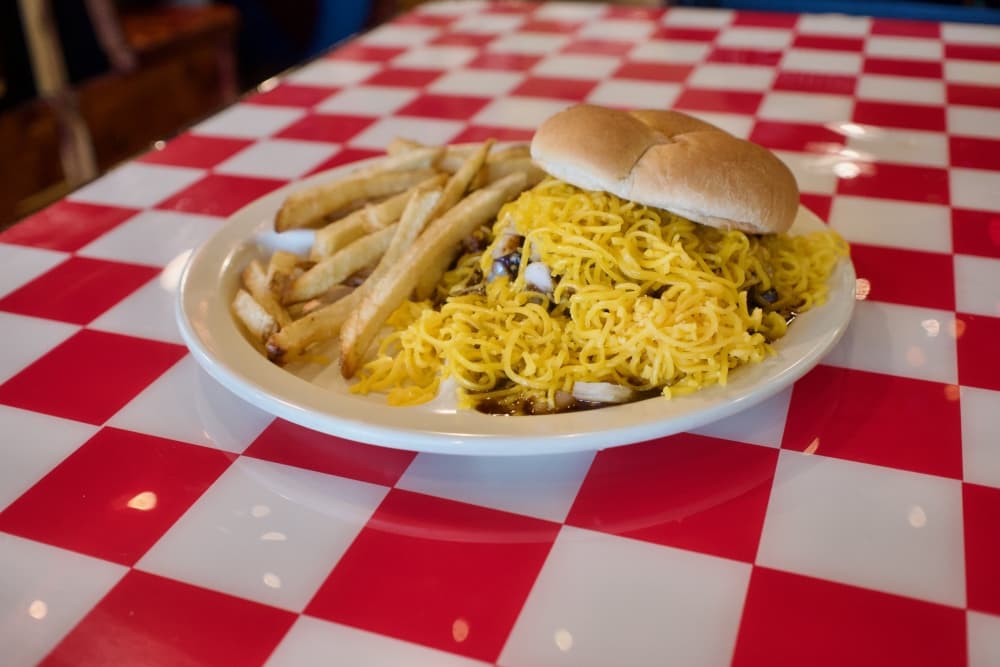 A hambuger swimming in hickory barbecue sauce, garnished with a healthy handful of cheddar cheese