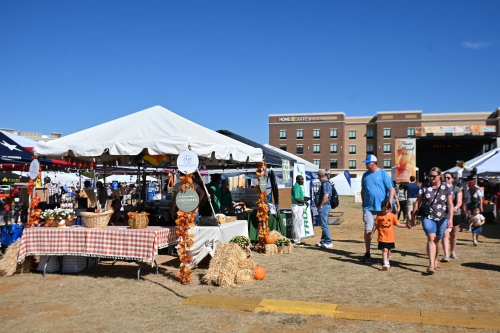 Attendees walk down a row of vendors at a festival