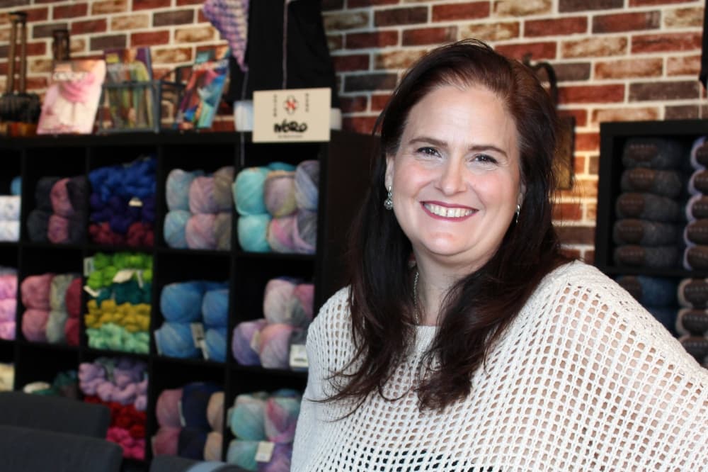 Female wearing a knit sweater stands in a yarn store. 