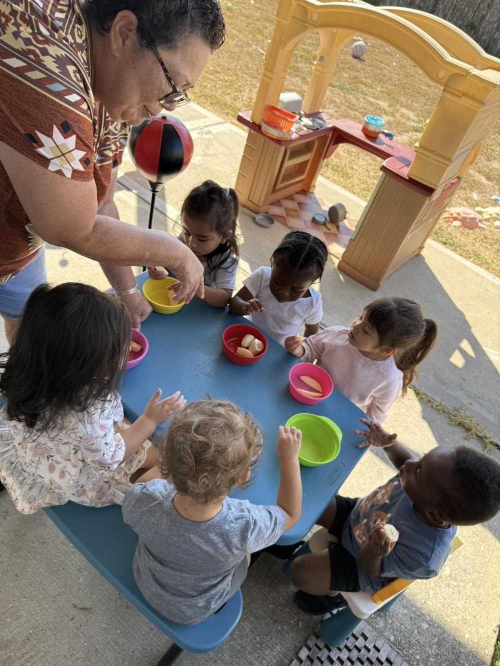 Child care worker interacting with children who are seated at a play table