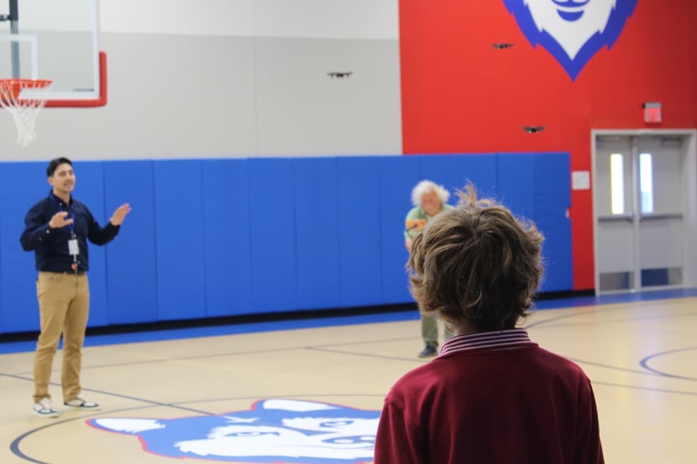 A little boy flys a drone in a school gym