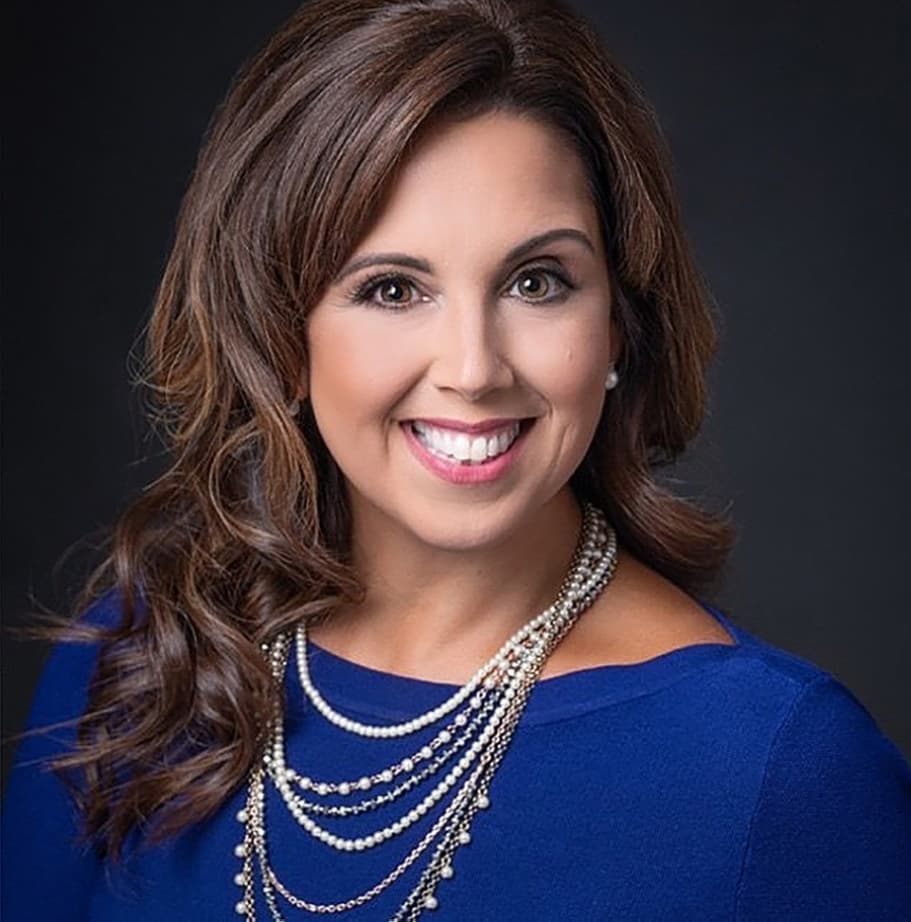 headshot portrait of a brunette woman wearing a blue top and necklaces