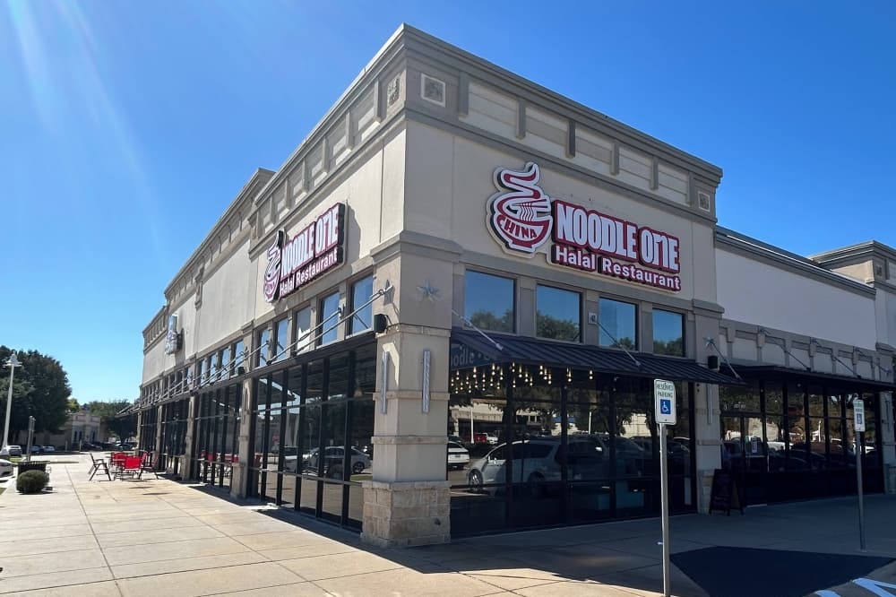 Exterior of a corner space in a strip mall featuring Noodle One signage. 