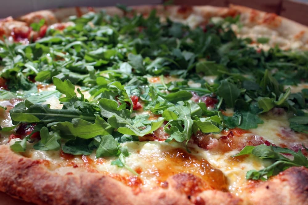 Pizza topped with cheese, red sauce and arugula. 