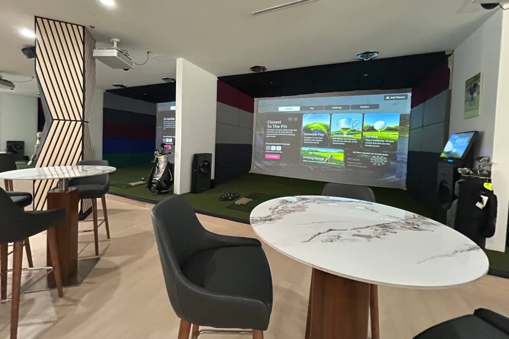 High tables and chairs next to a golf simulator bay. 