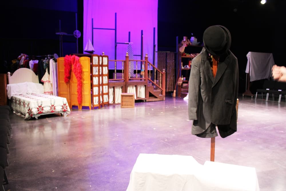 Mens jacket and hat hung on a rack center stage with other play props in the background.  