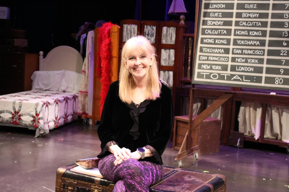 Female sitting on a trunk which is on a stage. 