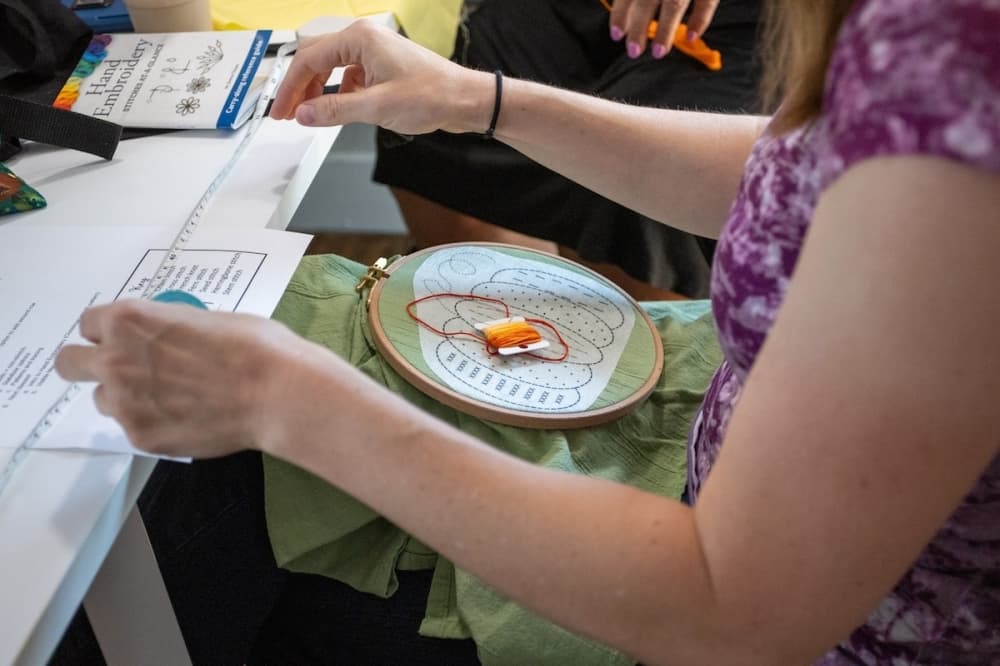 Students take part in a hand stitching class at Snippets, needling a pumpkin into a pillowcase.