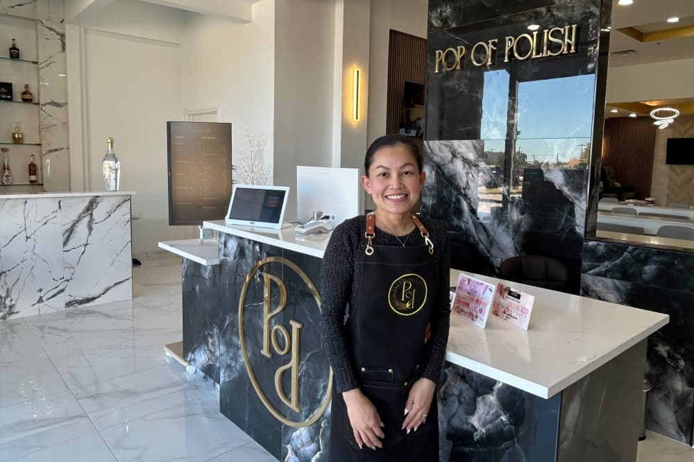 Female standing in front of a counter in a nail salon featuring Pop of Polish signage. 