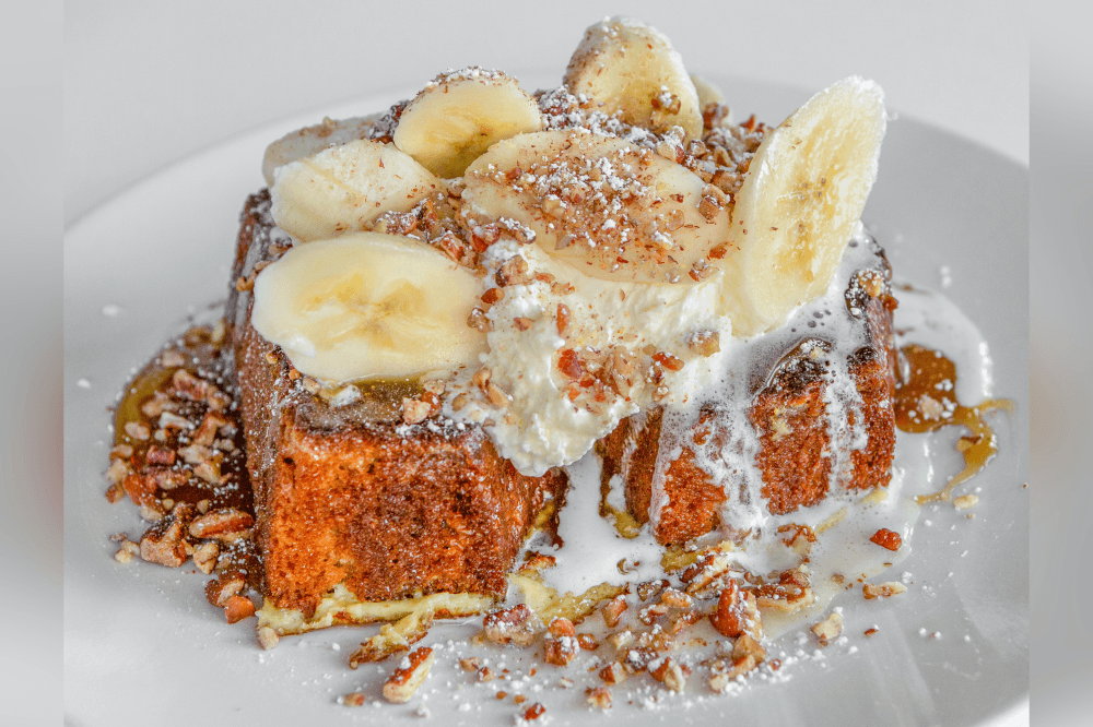 Bananas foster french toast from Phoebe’s Diner in Austin, Texas — thick slices of banana walnut bread topped with whipped cream, fresh bananas, pecans, bourbon caramel, and powdered sugar, a must-try brunch favorite for Austin comfort food and breakfast lovers.