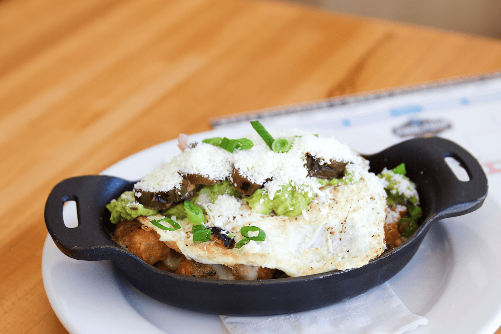 South First Tots from Phoebe’s Diner in Austin, Texas — golden tater tots topped with sage sausage gravy, mozzarella, fried egg, pickled chiles, guacamole, cotija cheese, and green onion, a popular gluten-free comfort food favorite for Austin brunch lovers.