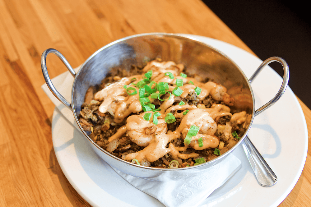 Shrimp and Grits from Phoebe’s Diner in Austin, Texas — sautéed shrimp with green pork chorizo, onions, mushrooms, corn, and goat cheese grits, topped with Hatch chile hollandaise and green onions, a popular gluten-free comfort food dish for Austin breakfast and brunch enthusiasts.